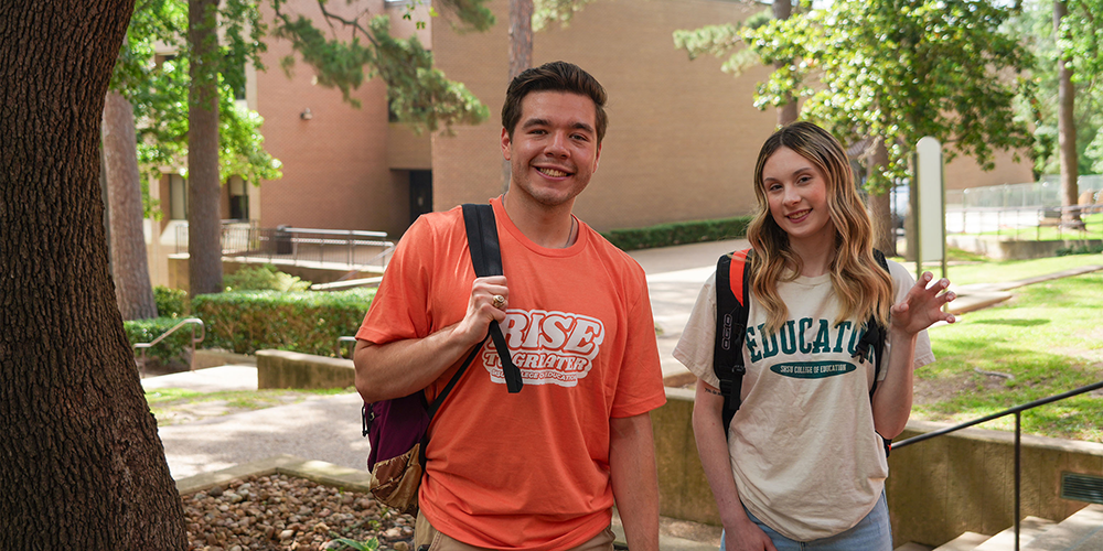 ​​Male college student and female college student smiling for photo outside of a brown brick building​ 