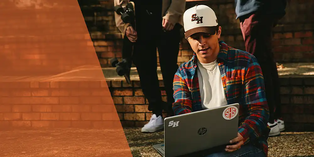 Student sitting and holding laptop with two other students in the background