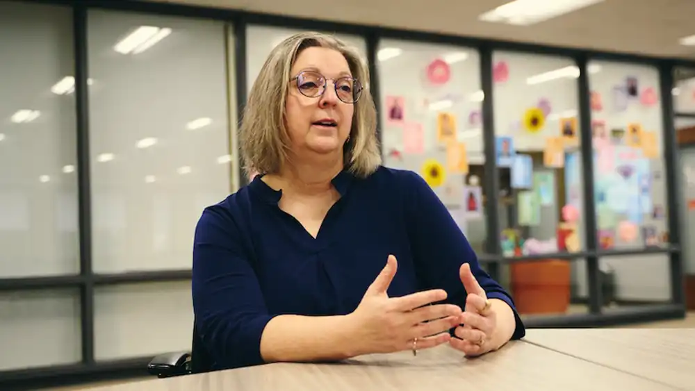Professor speaking to the camera in a classroom style class, with her hands opened.