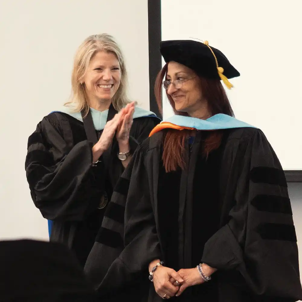 ​​Lady in regalia clapping for another lady dressed in regalia​ 
