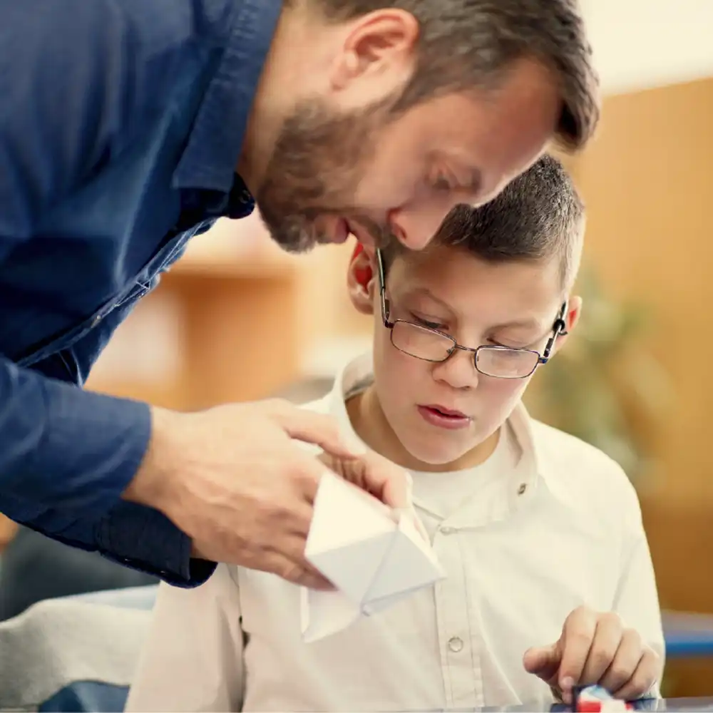 Man showing a young student how to fold a paper project