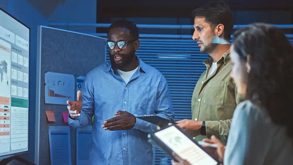Students collaborating on an AI and automation project, reviewing data visualizations on a large screen and using digital tablets in a modern classroom setting.