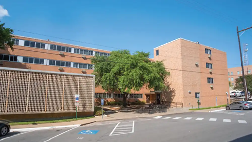 ​​Exterior view of Estill Hall at Sam Houston State University, a multi-story brick residence hall with shaded entry, large windows, and nearby accessible parking.​ 
