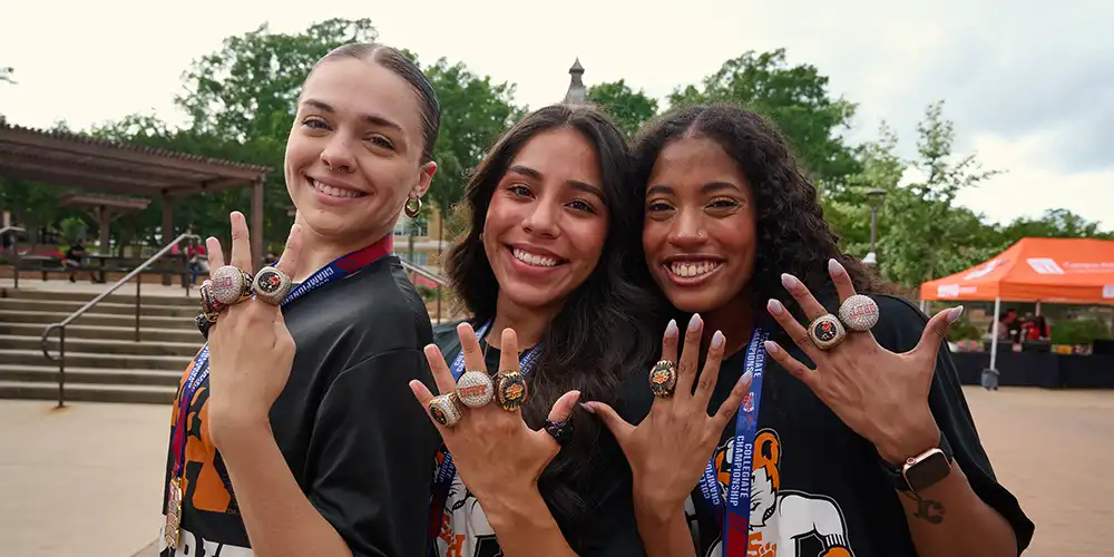 Panic at the Disco band members performing in the Johnson Coliseum at Sammypalooza with purple and yellow stage lighting and a large crowd in attendance. 