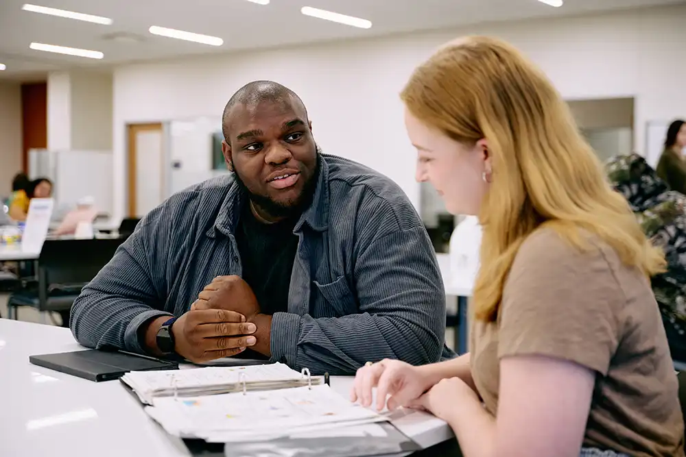 Male peer educator with female student client conversing at a dry erase table.