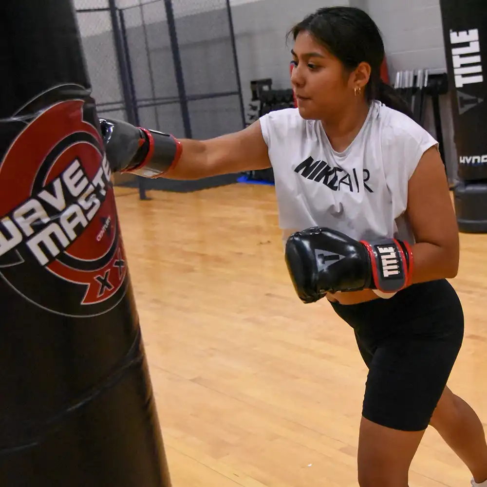 College girl wearing boxing gloves hitting standalone punching bag.
