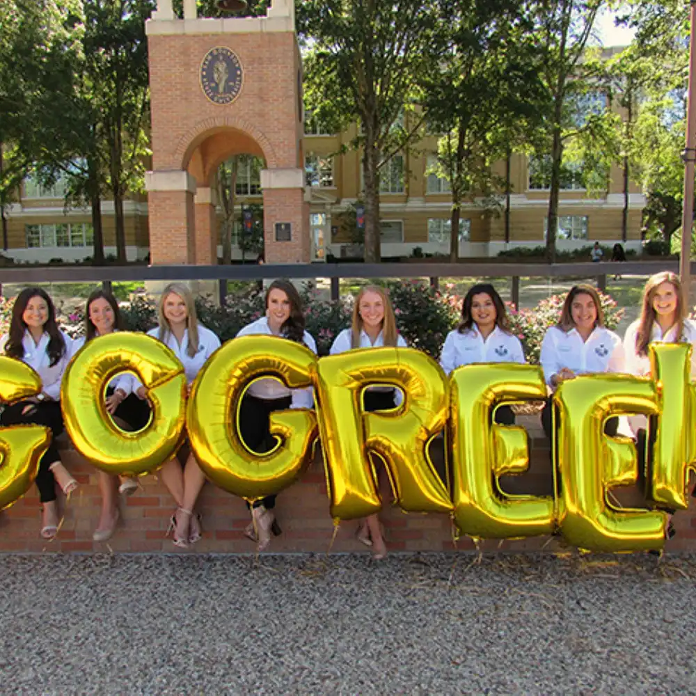 ​​Students holding balloons that spell out, “Go Greek”​ 