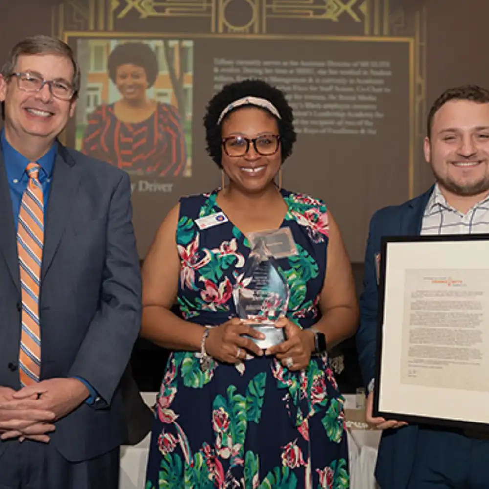​​Woman standing with two men after receiving the Keys of Excellence award.​ 