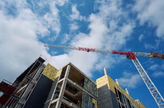 ​​Construction crane over the future Health Professions Building, with exposed concrete and insulation panels against a blue sky.​ 
