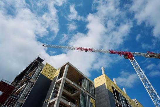 ​​Construction crane over the future Health Professions Building, with exposed concrete and insulation panels against a blue sky.​ 