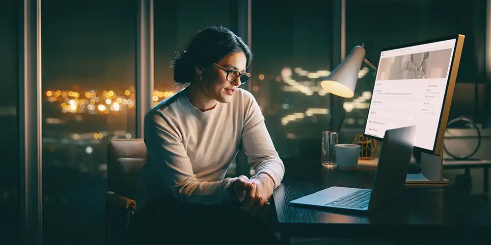 A woman sitting in a chair working on a laptop and computer..