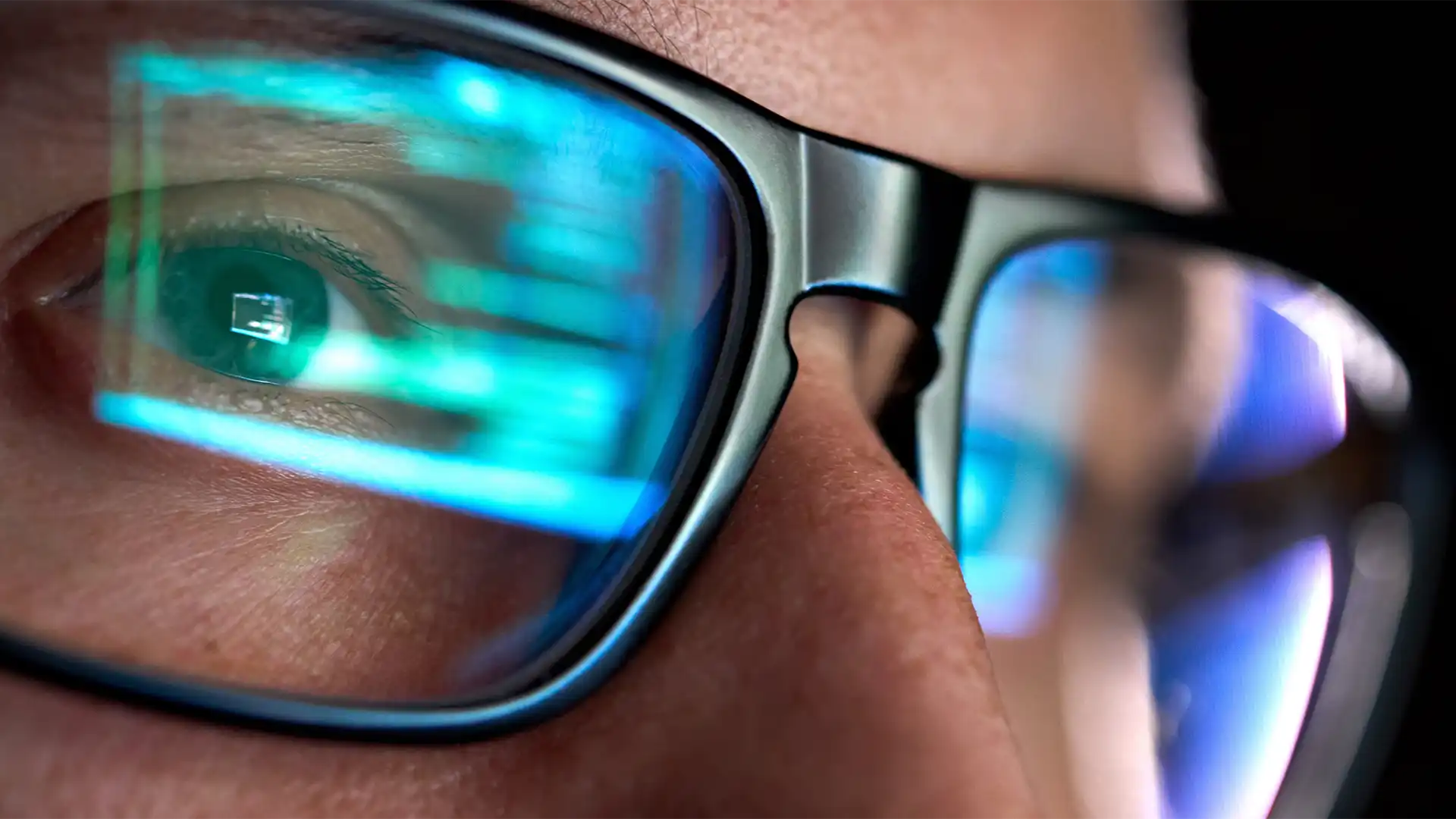 Close up of a person wearing glasses with digital media reflecting on their glasses. 
