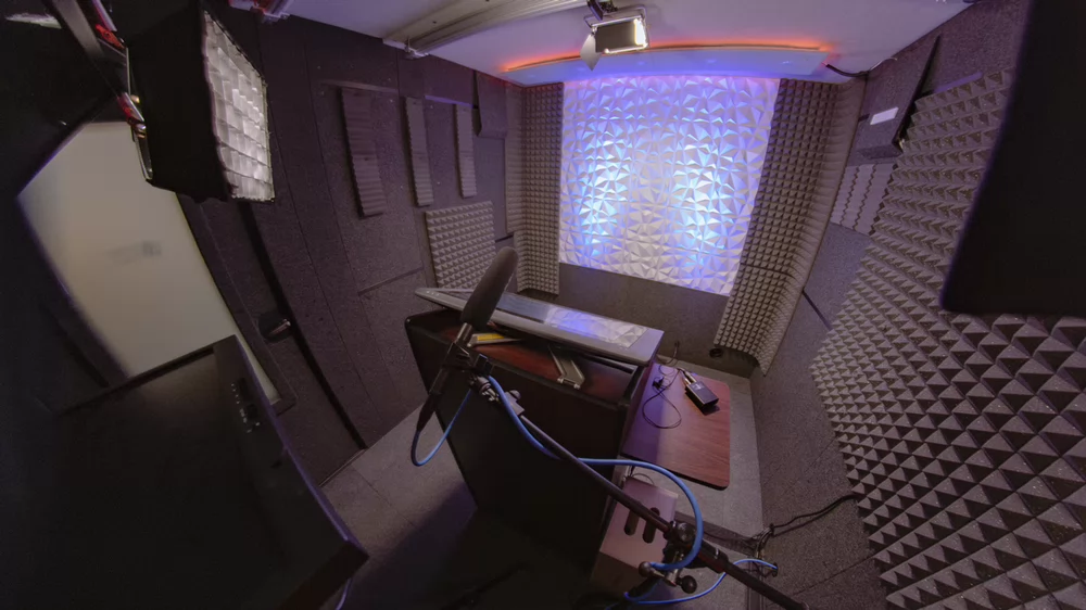 Soundproof studio with a Wacom tablet, with blue lighting on the back Wall. Studio lighting and a teleprompter is set up.