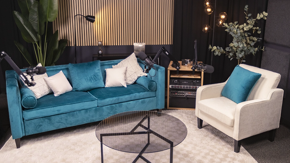 Podcast room with a jade covered couch and a white chair. a plant is in behind the couch.