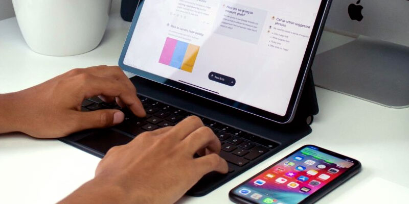 Hands typing on an ipad with a phone laying next to the ipad.