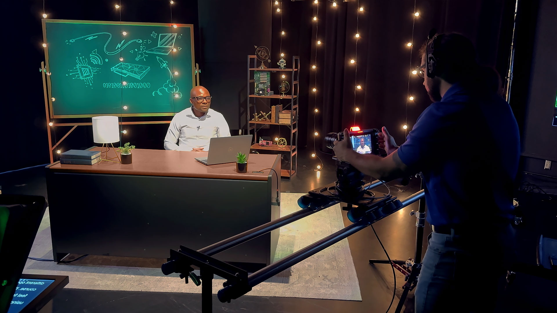 SamPoly instructor sits at a desk in a studio while a camera man captures lecture content for an online course.