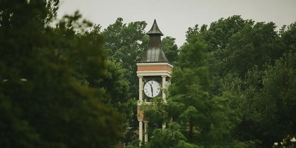 Iconic campus clock tower at Sam Houston State University partially hidden by trees on an overcast morning.