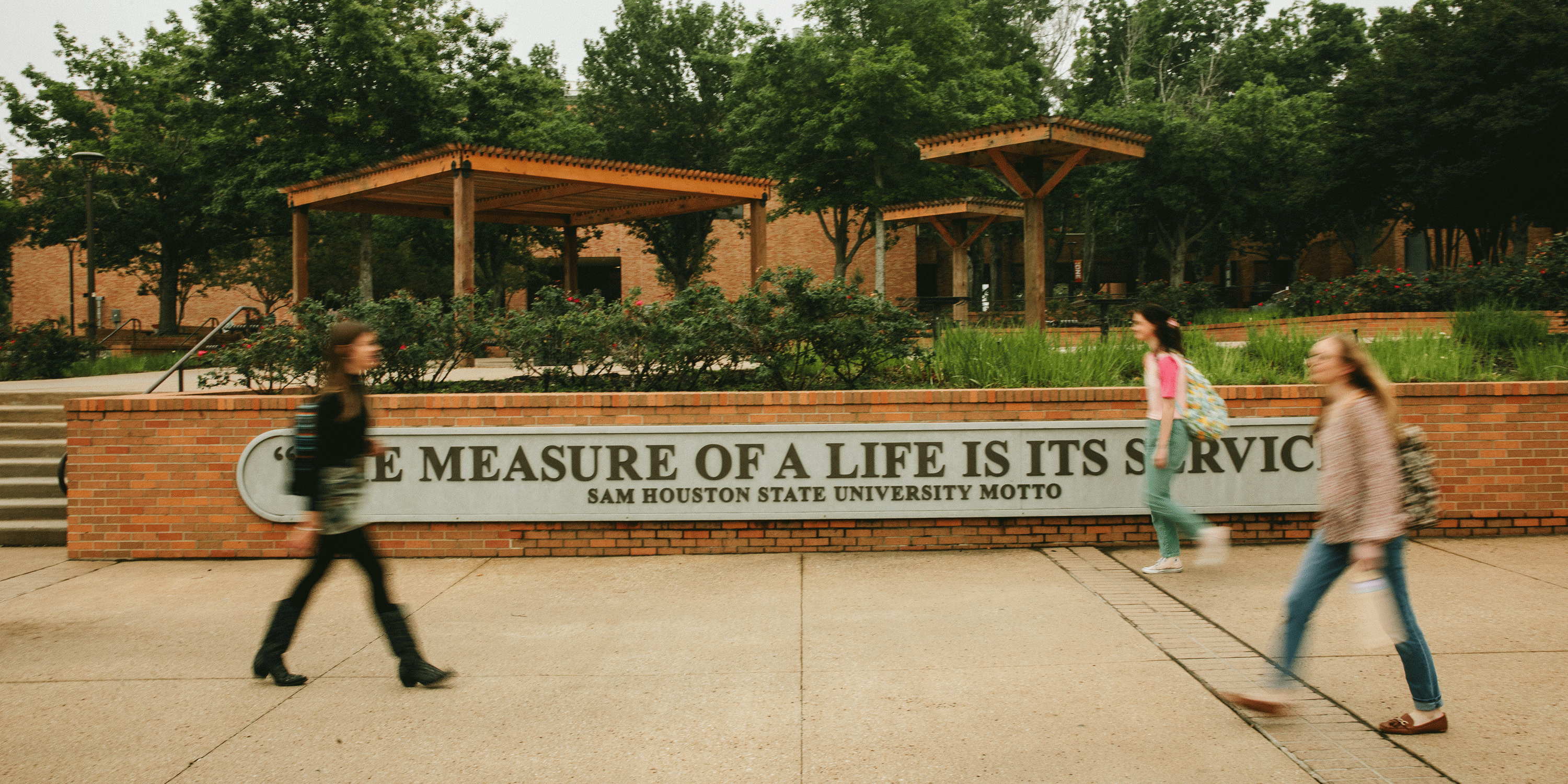 ​​Students walking past a sign with the university motto: the measure of a life is its service​ 