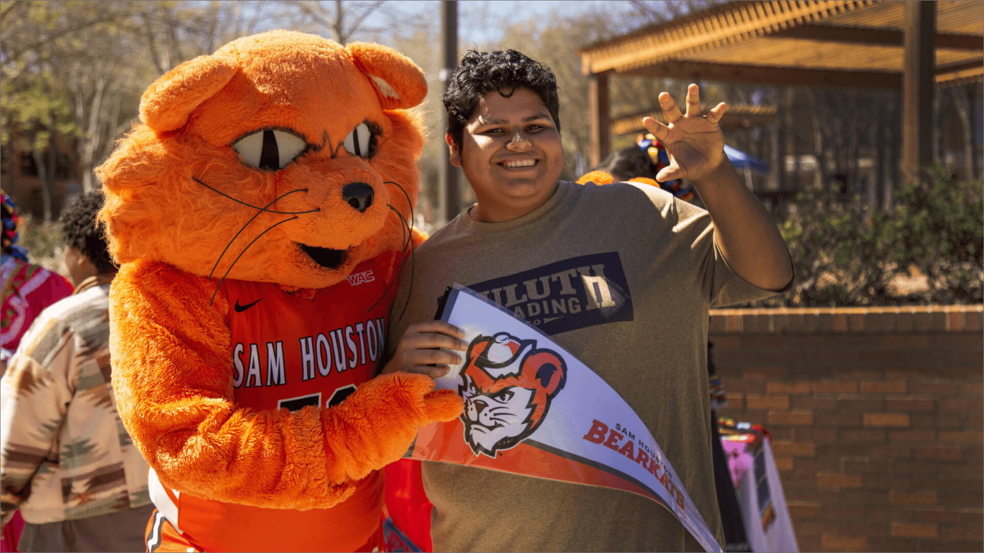 Sammy Bearkat standing with a student holding SHSU penant with hand up in claw form.